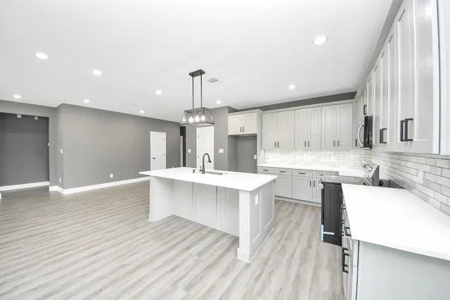 a large white kitchen with a large window a sink stainless steel appliances and cabinets