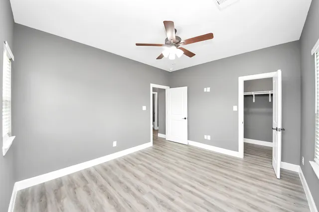 an empty room with wooden floor fan and windows