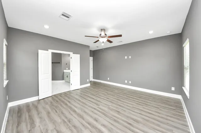 a view of an empty room with wooden floor and a ceiling fan