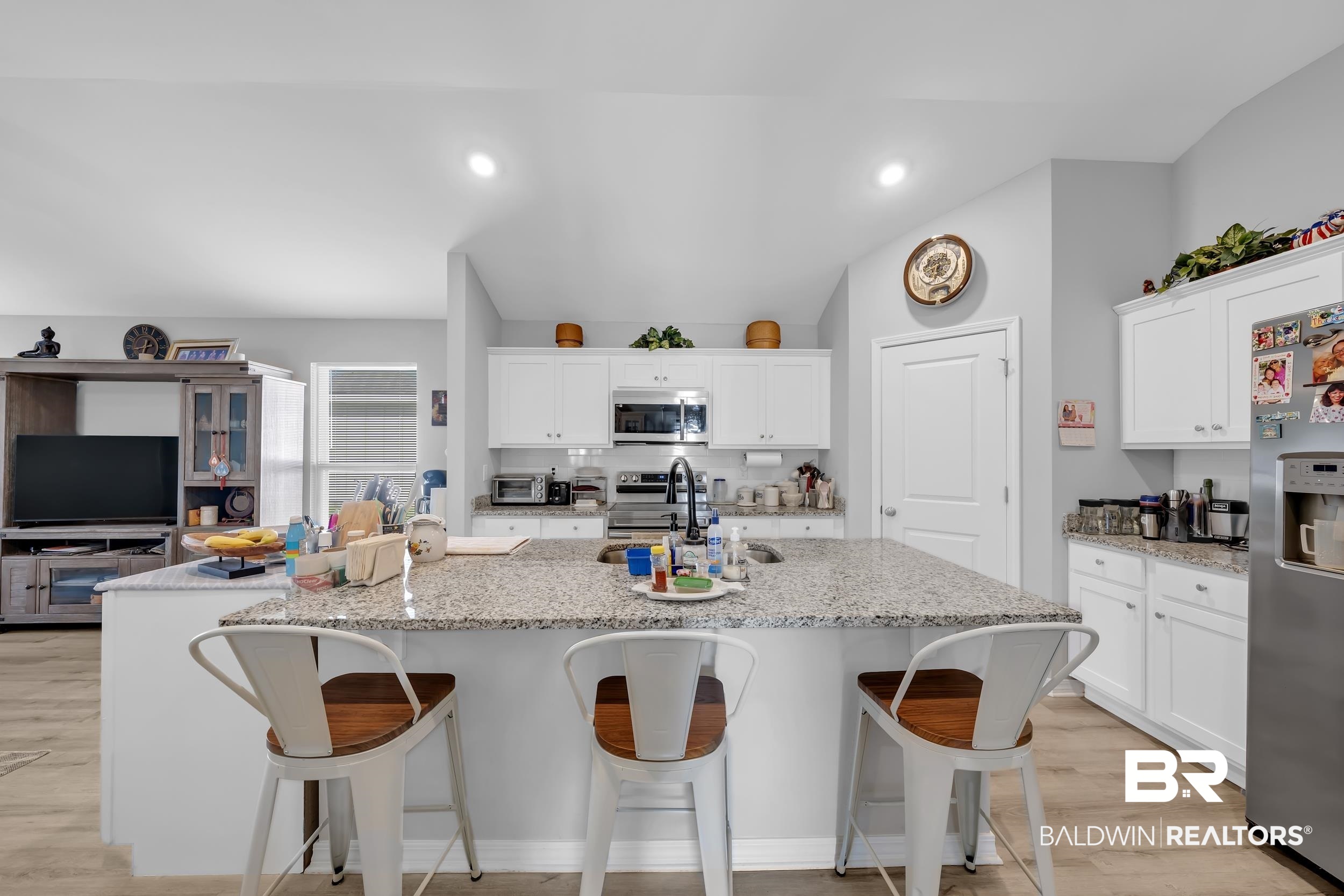 1228 Caper Avenue Foley, AL 36535 - Photo 9 of 54 Expansive kitchen island with granite countertop and seating for three, white cabinetry, integrated stainless steel appliances, and light wood-finish flooring