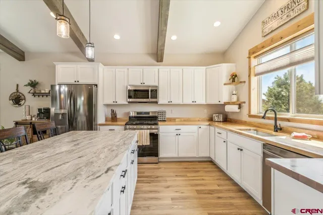 a large kitchen with stainless steel appliances kitchen island granite countertop a refrigerator a sink dishwasher a stove and white countertops with wooden floor
