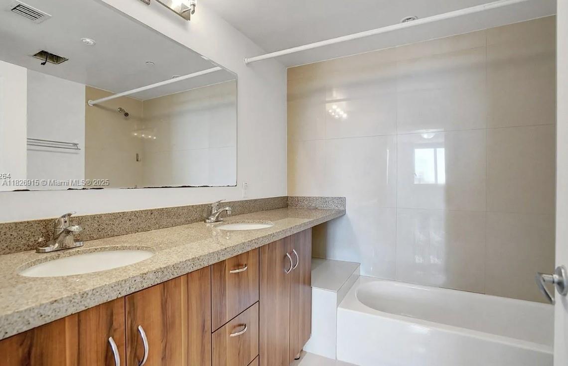 601 Northeast 23rd Street, Unit 1405 Miami, FL 33137 - Photo 15 of 23 a bathroom with a granite countertop sink a mirror a bathtub and shower