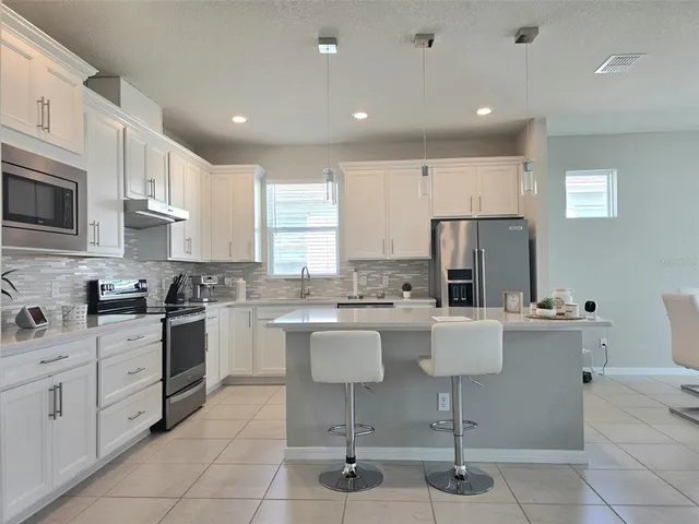 a kitchen with stainless steel appliances kitchen island granite countertop a refrigerator a stove a sink a dining table and chairs