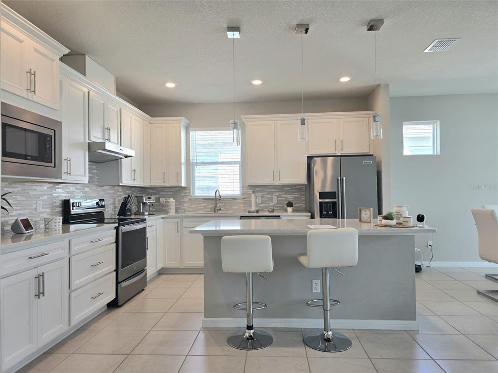 1973 Spring Shower Circle Kissimmee, FL 34744 - Photo 8 of 43 a kitchen with stainless steel appliances kitchen island granite countertop a refrigerator a stove a sink a dining table and chairs