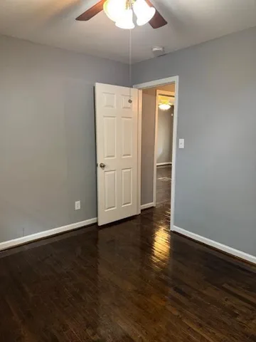 a view of an empty room with wooden floor and a ceiling fan