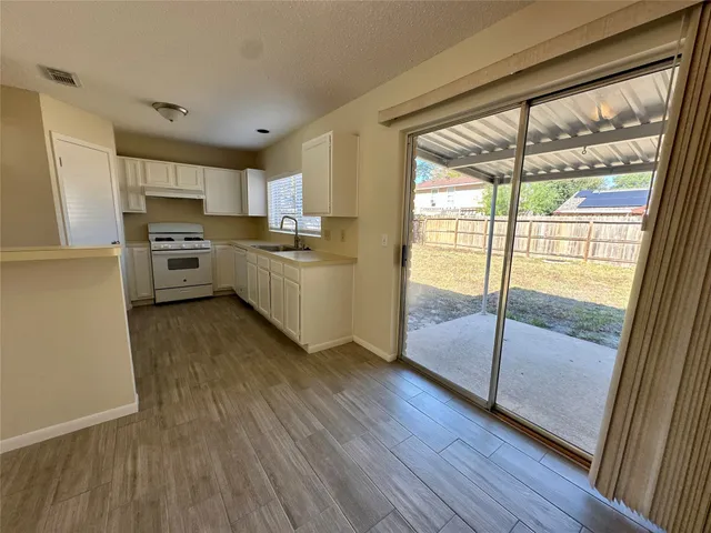 a kitchen with stainless steel appliances granite countertop a refrigerator a stove a sink and white cabinets with wooden floor