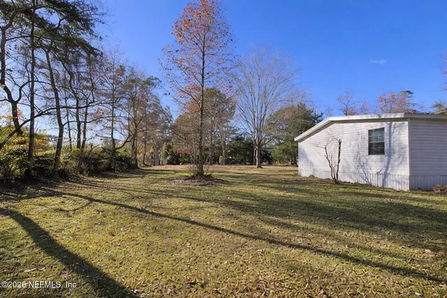 a view of a white house with a yard covered in the forest