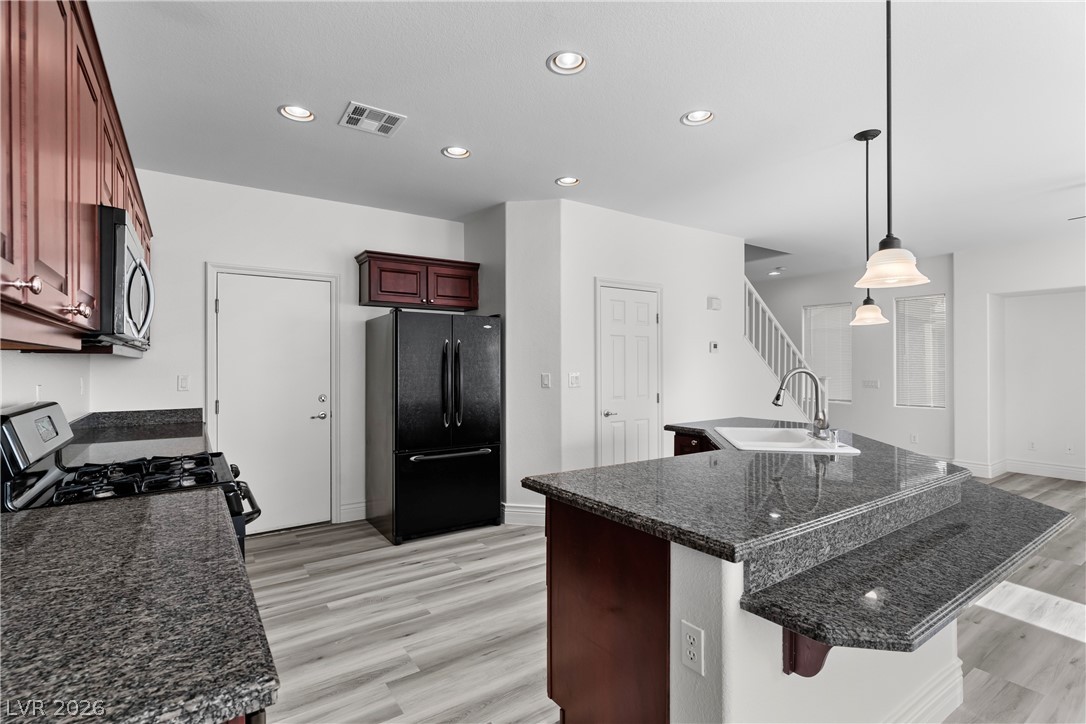 181 Short Ruff Way Las Vegas, NV 89148 - Photo 7 of 43 Kitchen with freestanding refrigerator, light wood finished floors, an island with sink, range with gas stovetop, and dark stone countertops