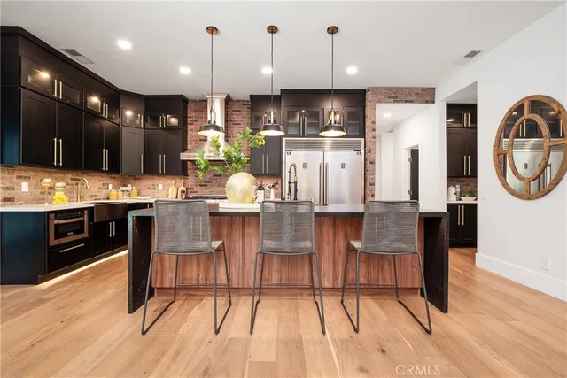 a kitchen with stainless steel appliances kitchen island granite countertop a refrigerator a stove top oven and a dining table with wooden floor