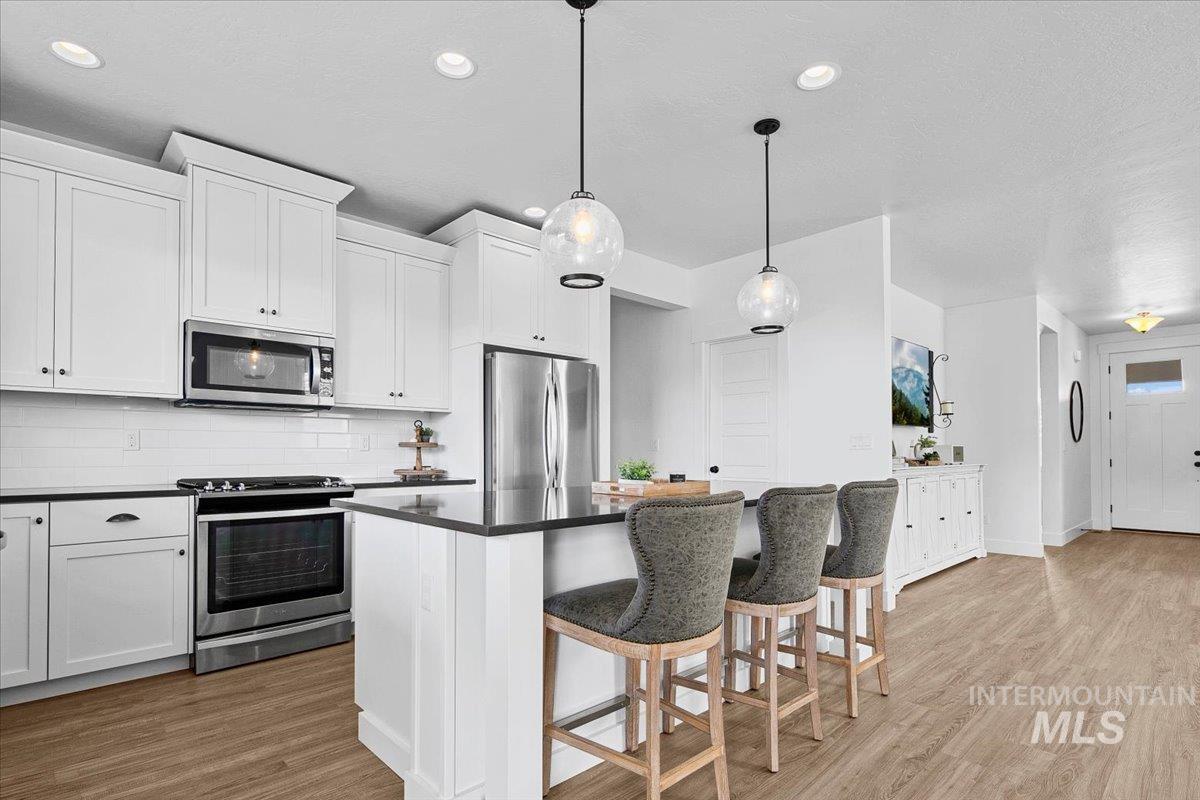 2085 North Concha Court Middleton, ID 83644 - Photo 13 of 37 Kitchen with stainless steel appliances, light wood finished floors, a kitchen breakfast bar, decorative light fixtures, and tasteful backsplash