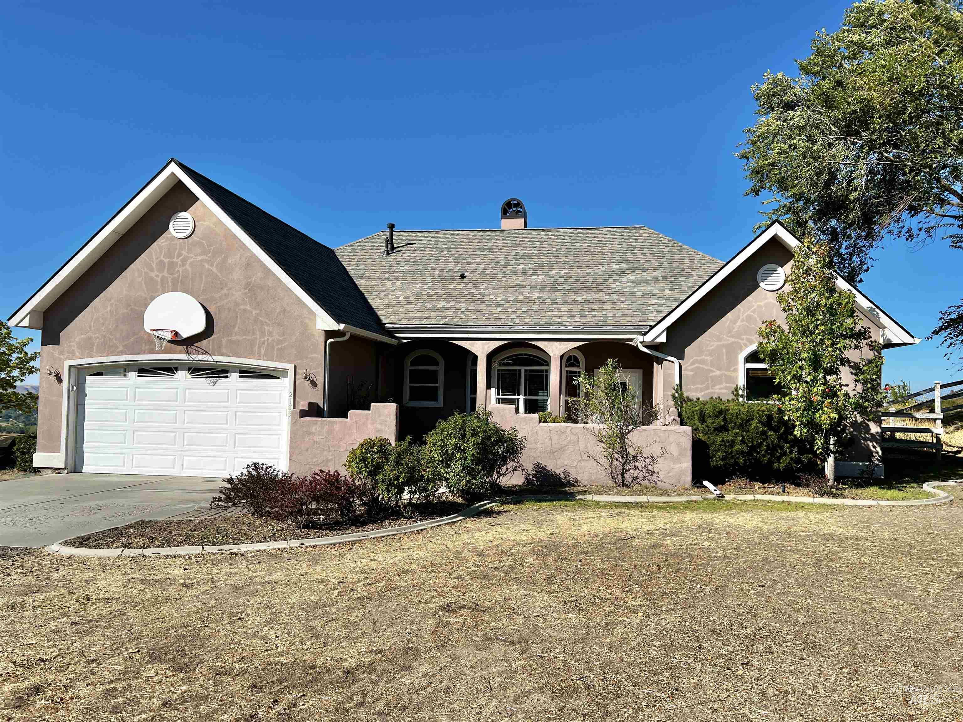 Stucco exterior with a pitched roof, attached garage, arched entryways, and mature landscaping