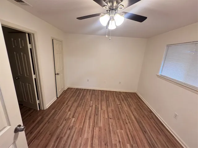 a view of an empty room with wooden floor and a ceiling fan