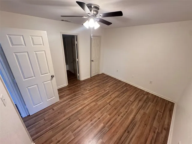 a view of an empty room with wooden floor and a ceiling fan