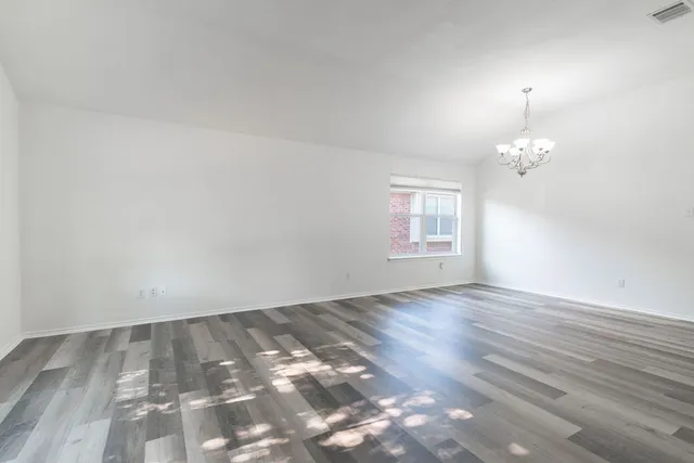 an empty room with wooden floor chandelier and windows