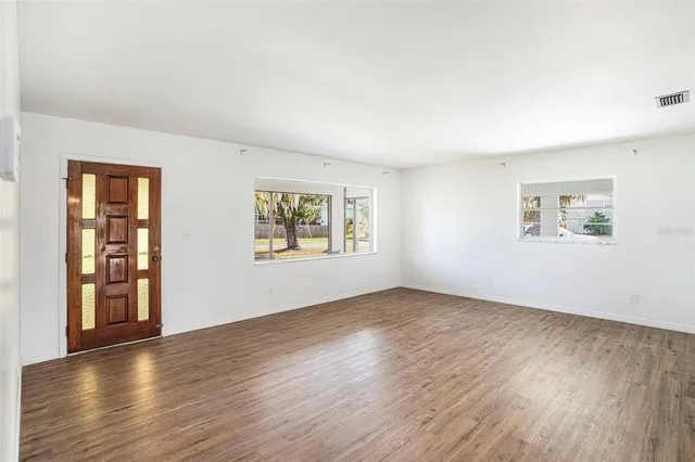 a view of an empty room with wooden floor and a window