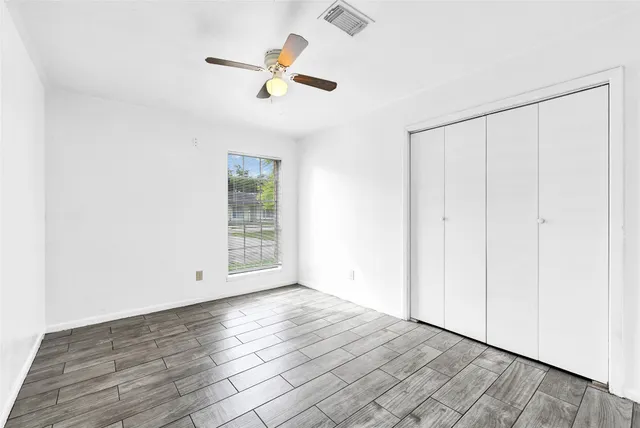an empty room with wooden floor closet and windows