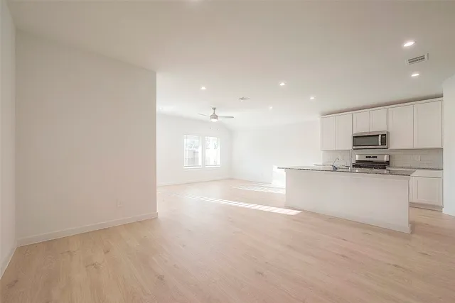 a view of kitchen with kitchen island granite countertop a stove top oven a sink and white cabinets