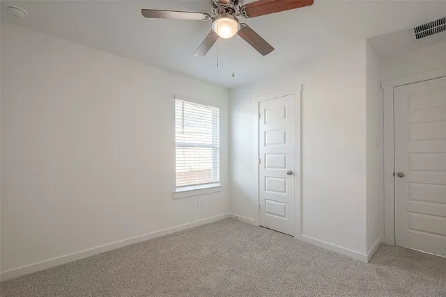 an empty room with chandelier fan and windows