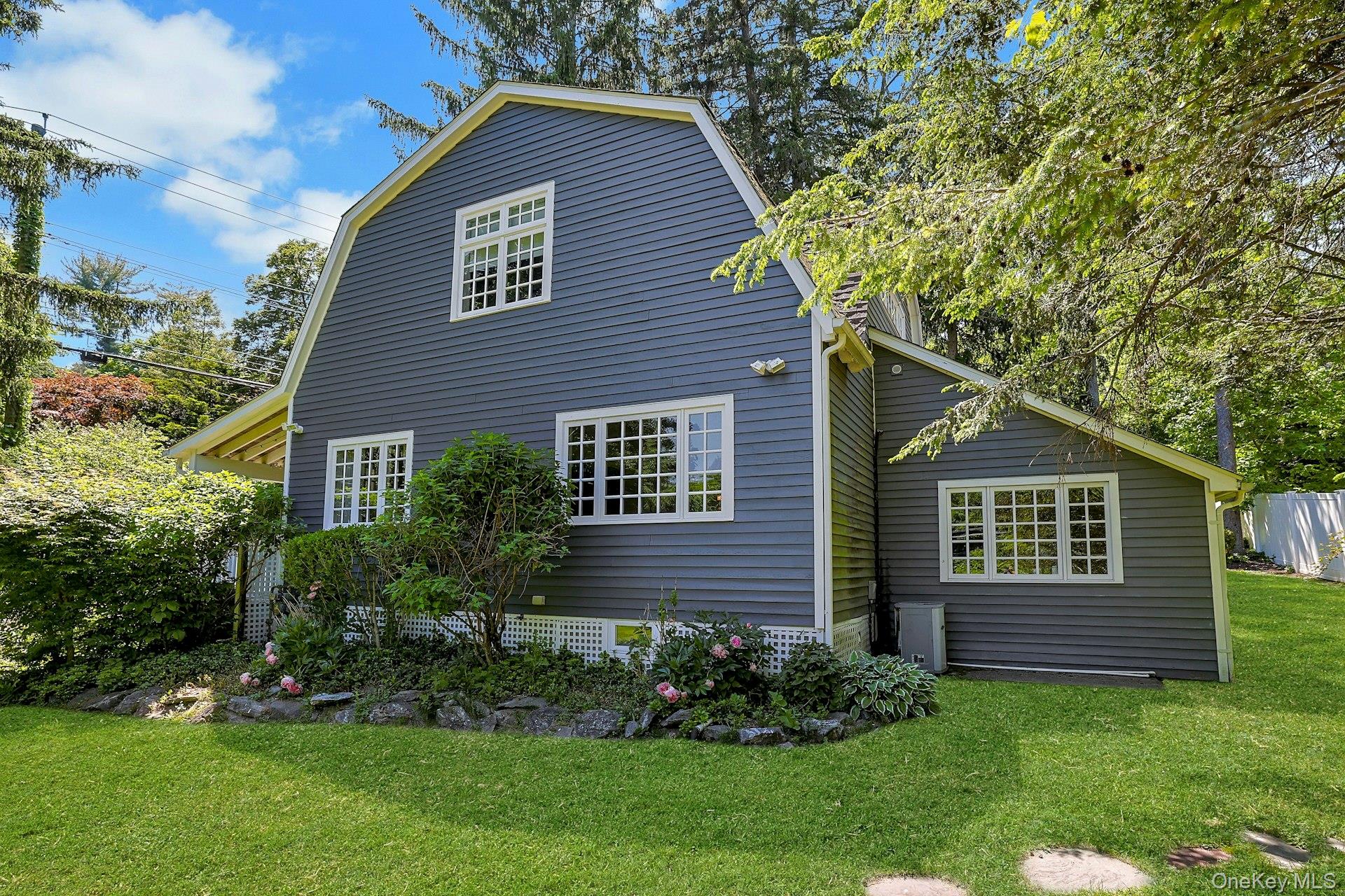 65 Douglas Road Chappaqua, NY 10514 - Photo 39 of 41 A beautifully landscaped side view of the home highlights the property’s natural charm, with lush greenery and thoughtfully designed grounds.