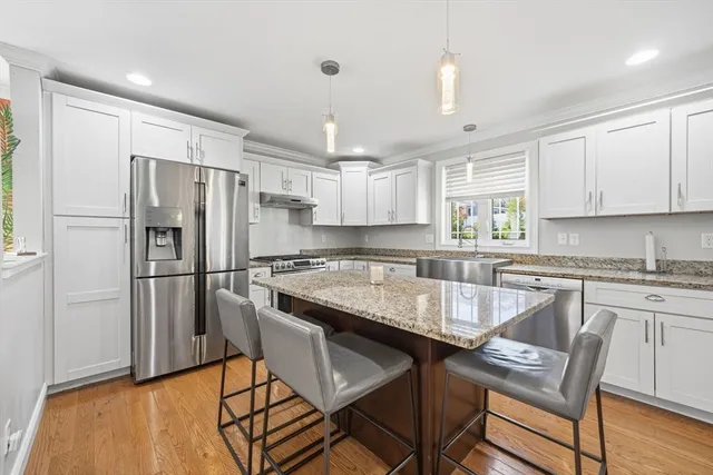 a kitchen with granite countertop a refrigerator a stove a sink and white cabinets with wooden floor