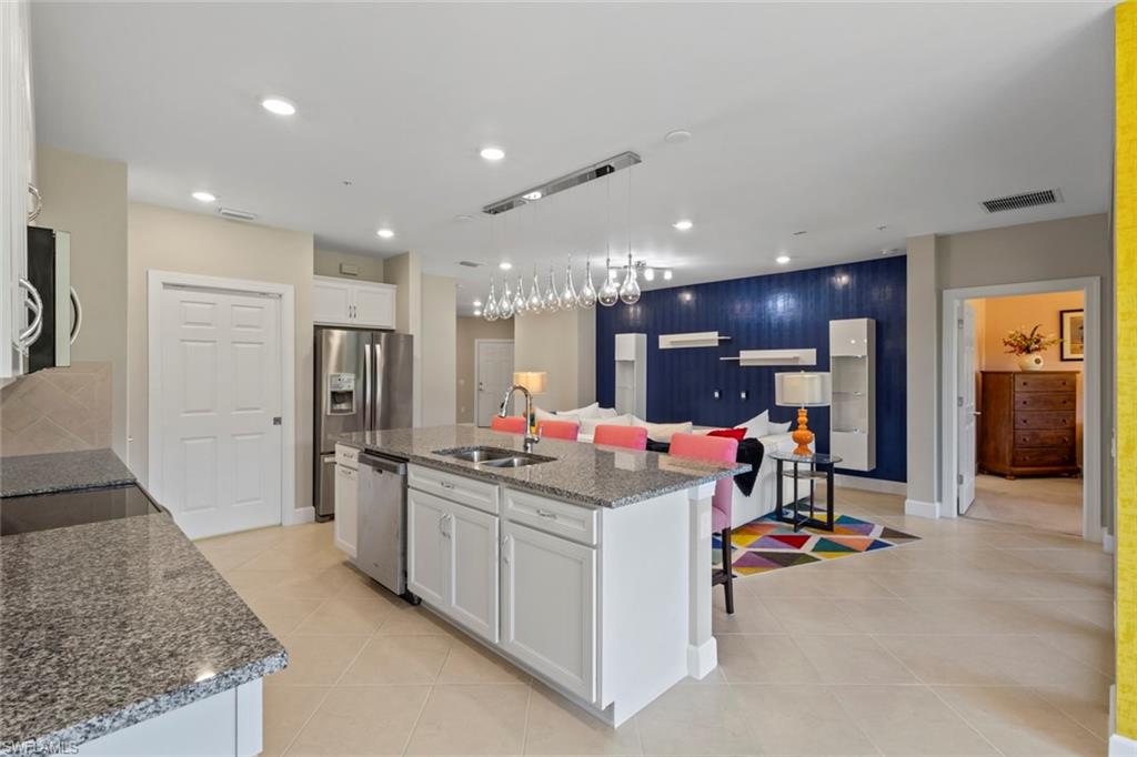 a room with stainless steel appliances kitchen island granite countertop a refrigerator and a sink