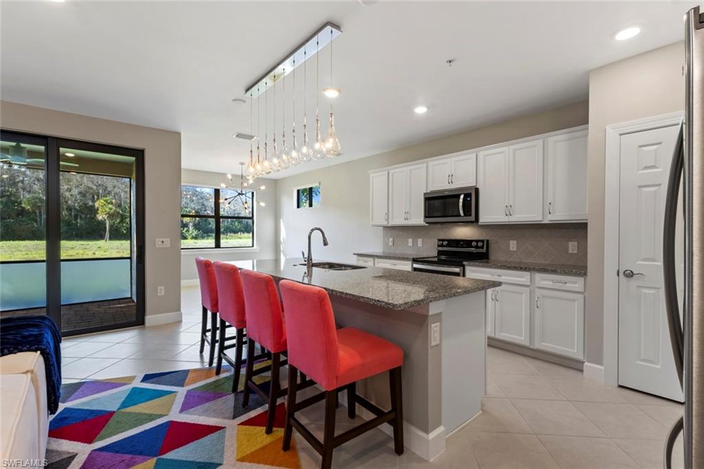 5701 Mayflower Way, Unit 1302 Ave Maria, FL 34142 - Photo 3 of 32 a kitchen with stainless steel appliances granite countertop a dining table chairs refrigerator and sink