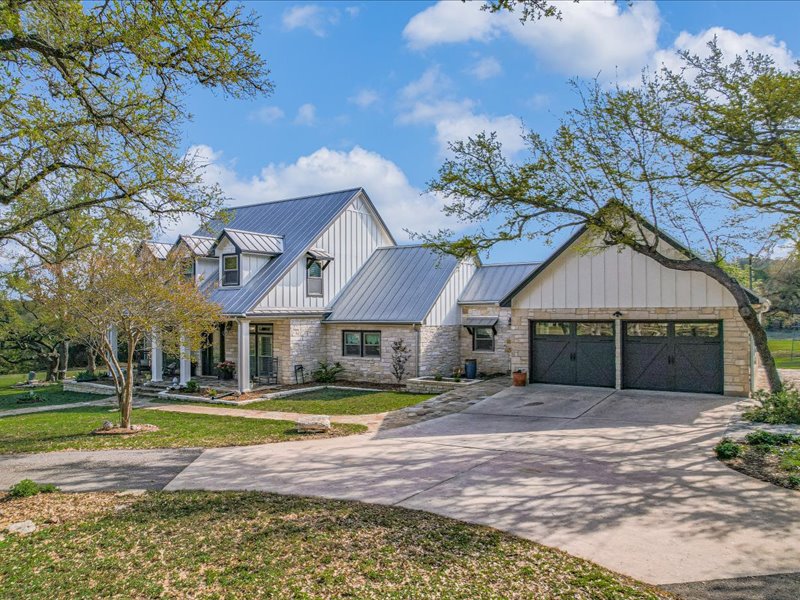 14036 Timberline Trail Austin, TX 78737 - Photo 2 of 40 Modern farmhouse style home featuring a standing seam metal roof, concrete driveway, stone siding, covered porches.
