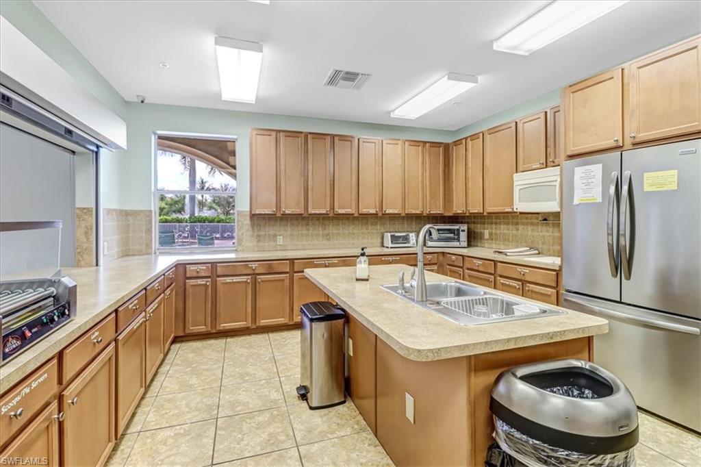 14130 Winchester Court, Unit 1503 Naples, FL 34114 - Photo 32 of 39 Kitchen with sink, a kitchen island with sink, stainless steel refrigerator, and light tile floors