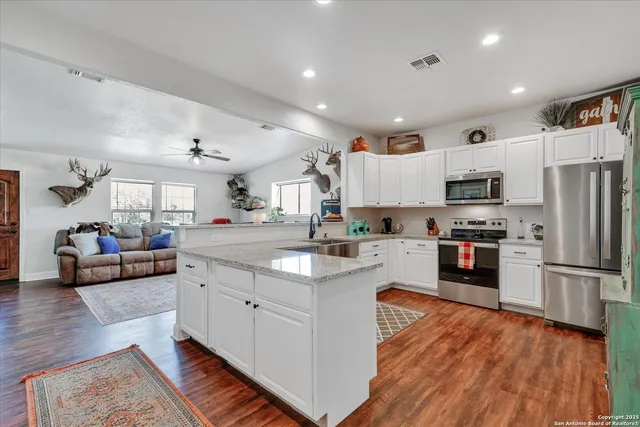 a large white kitchen with stainless steel appliances granite countertop a couch and a view of living room