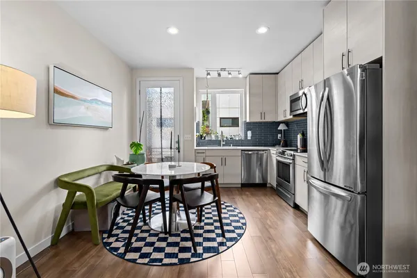 a kitchen with stainless steel appliances granite countertop a dining table chairs refrigerator and sink
