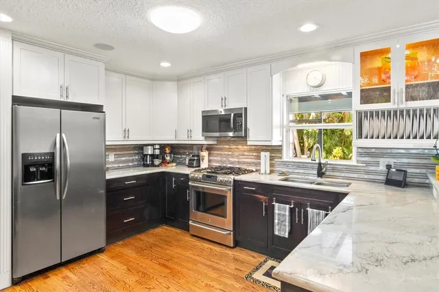 a kitchen with stainless steel appliances granite countertop a stove top oven a sink dishwasher a refrigerator and a dining table with wooden cabinet
