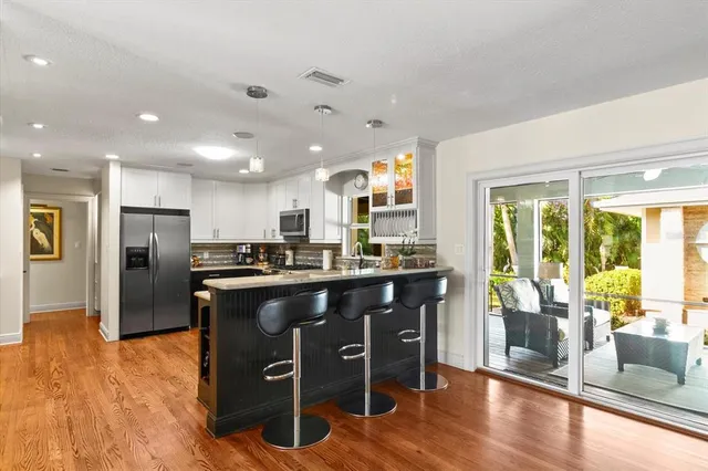 a kitchen with stainless steel appliances granite countertop a refrigerator a sink dishwasher a stove and a dining table with wooden floor