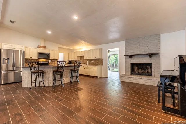 a living room with stainless steel appliances furniture a fireplace a flat screen tv and kitchen view