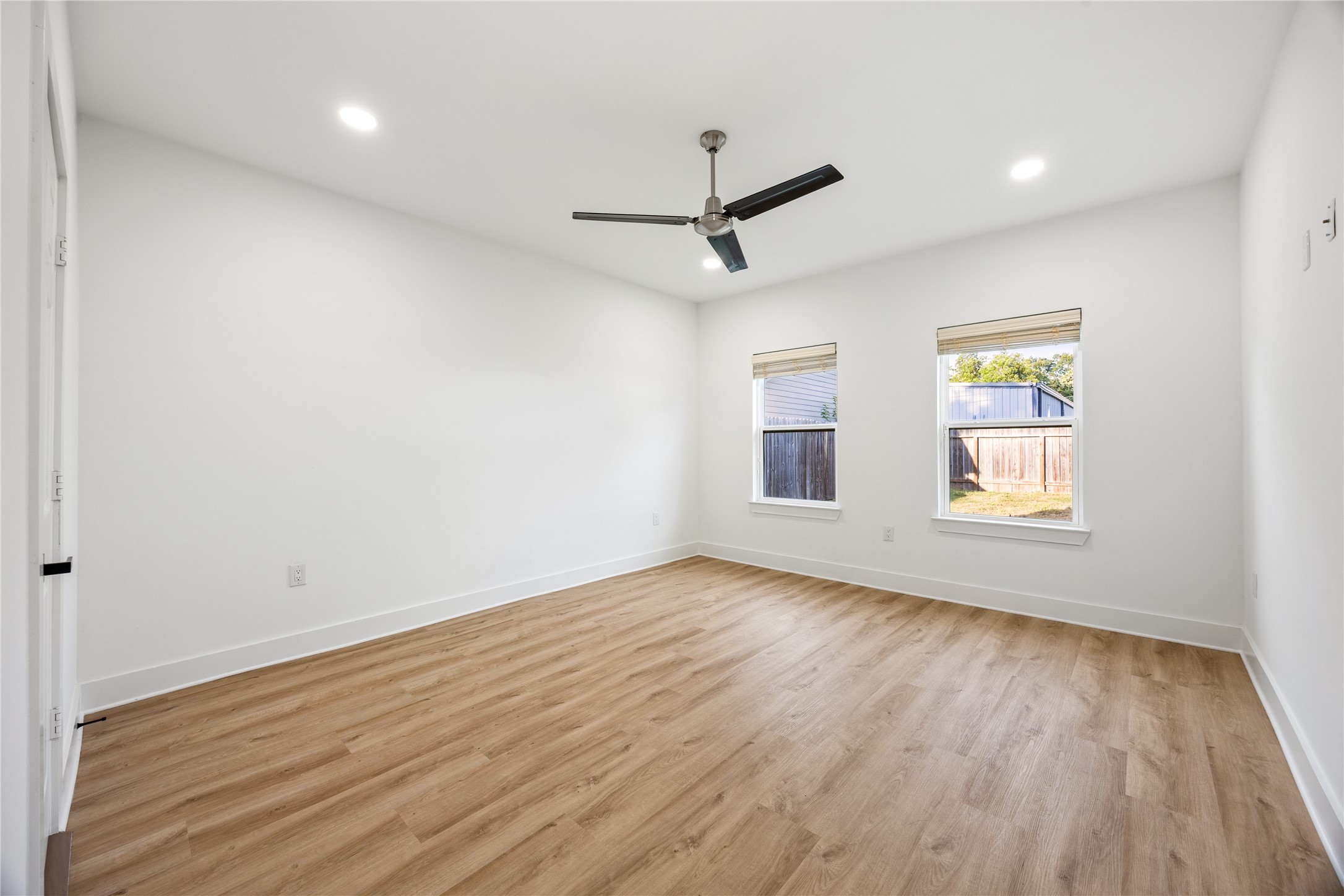 1121 Austin Street Rosenberg, TX 77471 - Photo 25 of 44 This is a bright, modern bedroom featuring clean white walls, luxury vinyl flooring, recessed lighting, and a ceiling fan. Two windows provide natural light and a view of the backyard.