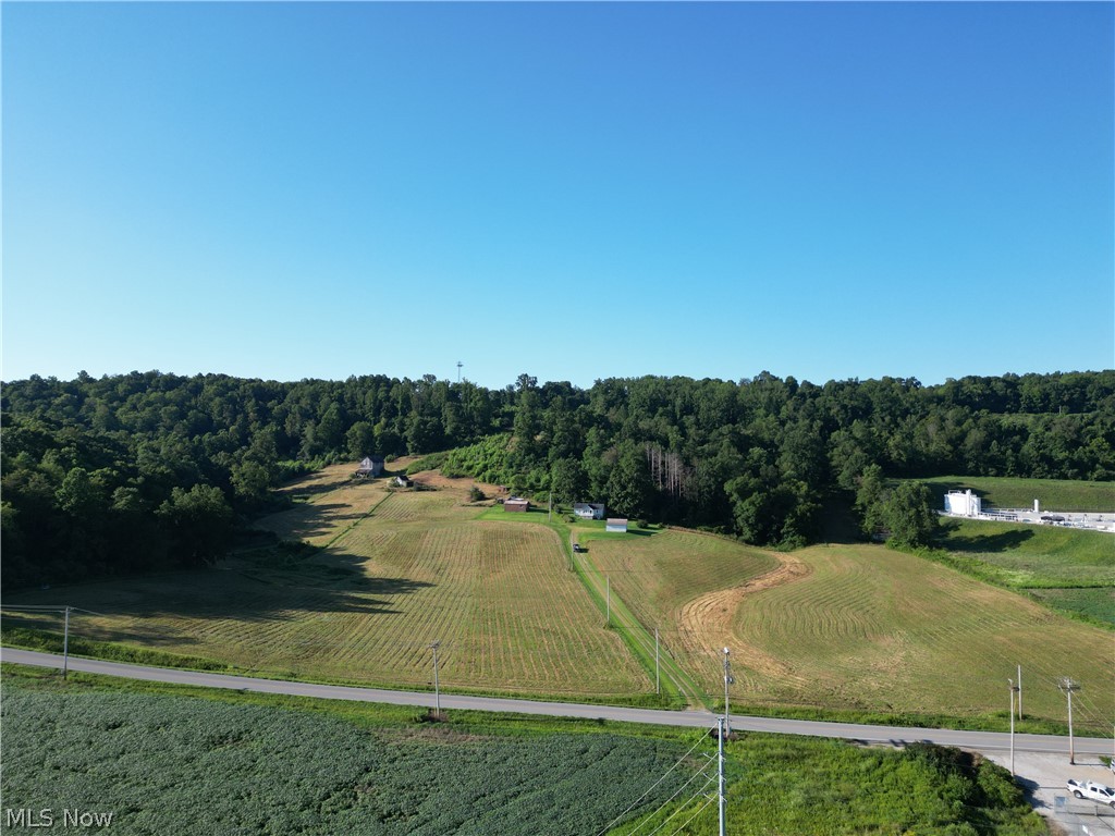 Expansive land parcel featuring cultivated fields, mature tree lines, and a paved road frontage