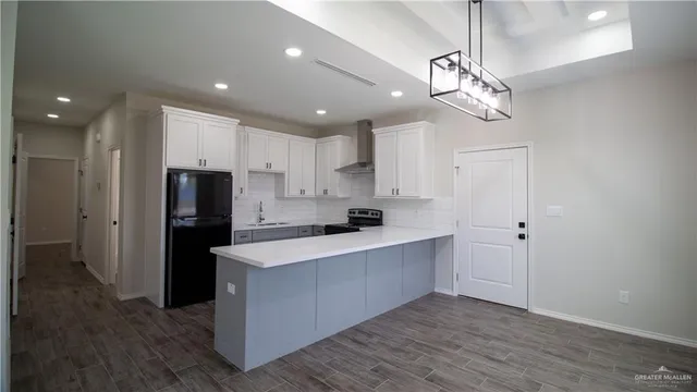 a large kitchen with stainless steel appliances a refrigerator oven a sink dishwasher and white cabinets with wooden floor