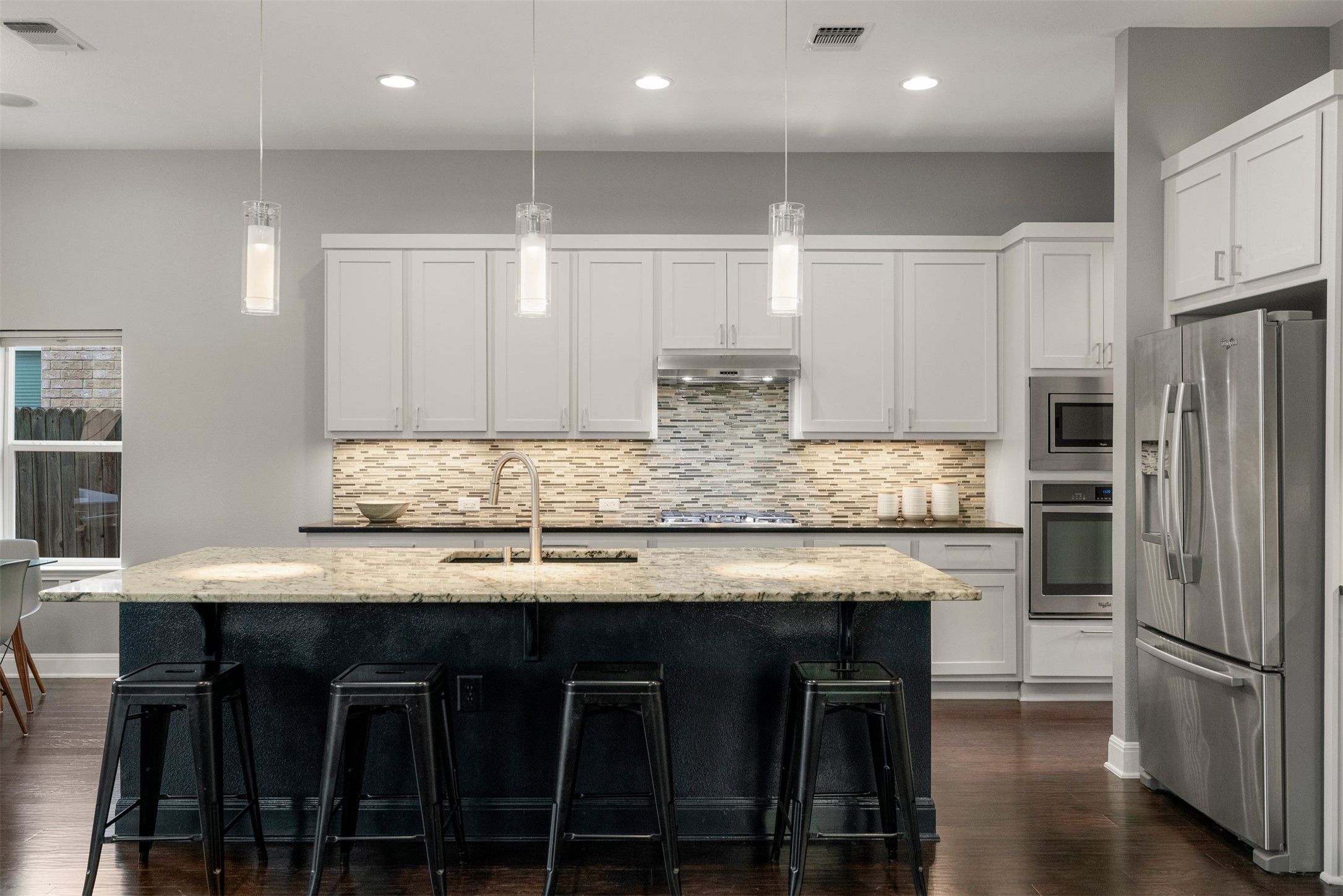 4512 Ruiz Street Austin, TX 78723 - Photo 16 of 40 The kitchen finishes bring everything together with shaker-style cabinetry, a tile backsplash, and pendant lighting hanging above the 9 ft granite center island, adding detail and warmth to the space while highlighting the main gathering area of the kitchen