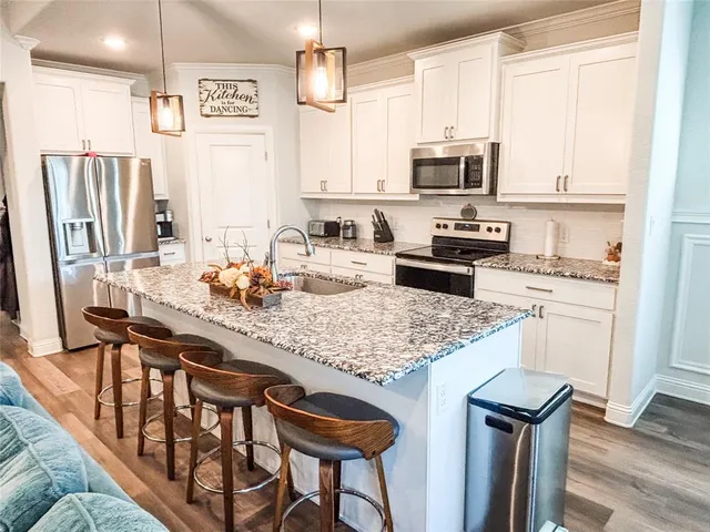 a kitchen with stainless steel appliances granite countertop a stove a refrigerator a sink a dining table and chairs with wooden floor