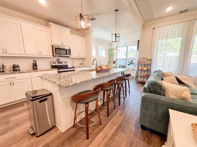 a living room with stainless steel appliances kitchen island granite countertop furniture a kitchen island a stove a sink a dining table and chairs with wooden floor