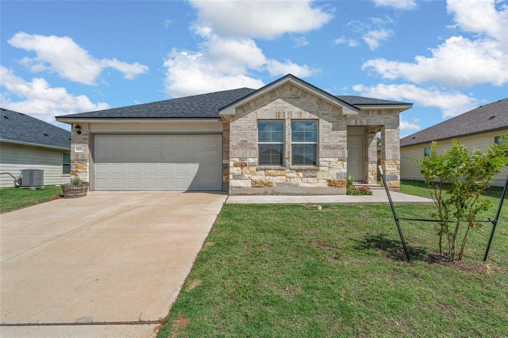 View of front of property with concrete driveway, a garage, a front yard, a shingled roof, and stone siding