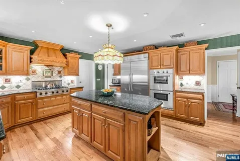 a kitchen with stainless steel appliances granite countertop wooden cabinets a stove a sink and dishwasher a refrigerator with wooden floor