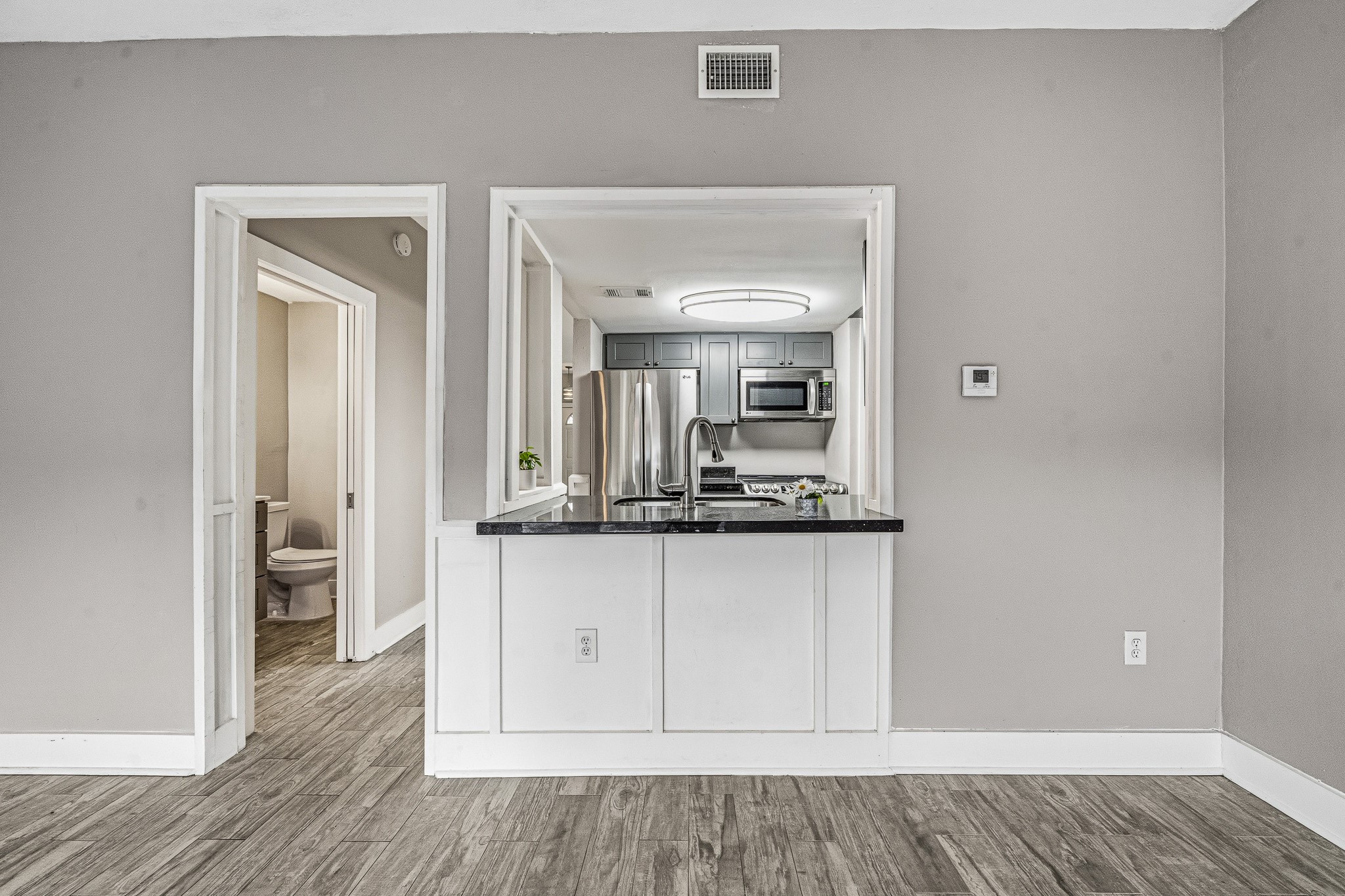 830 Threadneedle Street, Unit 240 Houston, TX 77079 - Photo 15 of 33 This photo showcases a modern kitchen with stainless steel appliances, a sleek countertop, and an open pass-through window. Adjacent is a doorway leading to a bathroom. The space features light gray walls and wood-look flooring, creating a clean and contemporary feel.