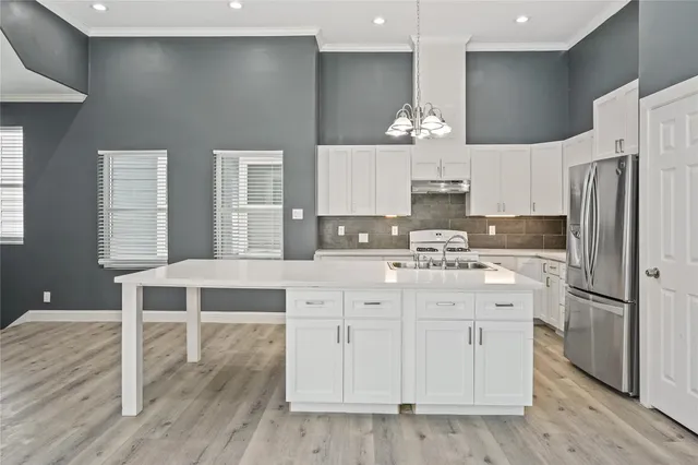 a kitchen with stainless steel appliances kitchen island granite countertop a stove a sink a refrigerator and white cabinets with wooden floor