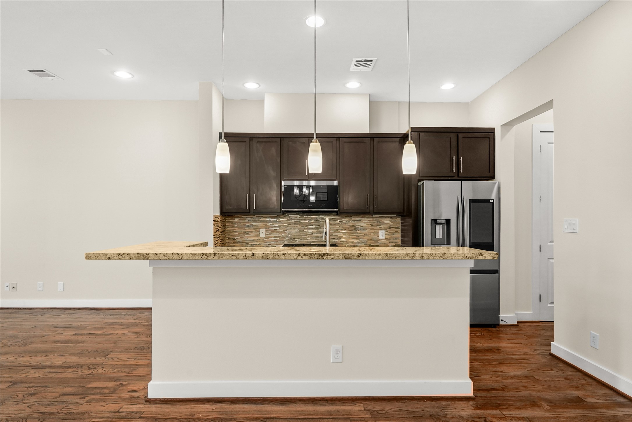 4409 Schuler Street, Unit A Houston, TX 77007 - Photo 12 of 33 The kitchen island showcases a granite countertop atop a neutral base, illuminated by three pendant lights overhead, while dark cabinetry above offers ample storage.