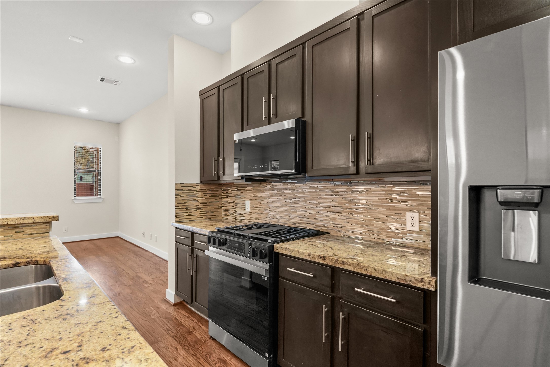4409 Schuler Street, Unit A Houston, TX 77007 - Photo 14 of 33 Close-up details show the tile backsplash and granite countertops surrounding the gas range and microwave. Dark wood cabinetry provides ample storage options for the kitchen.