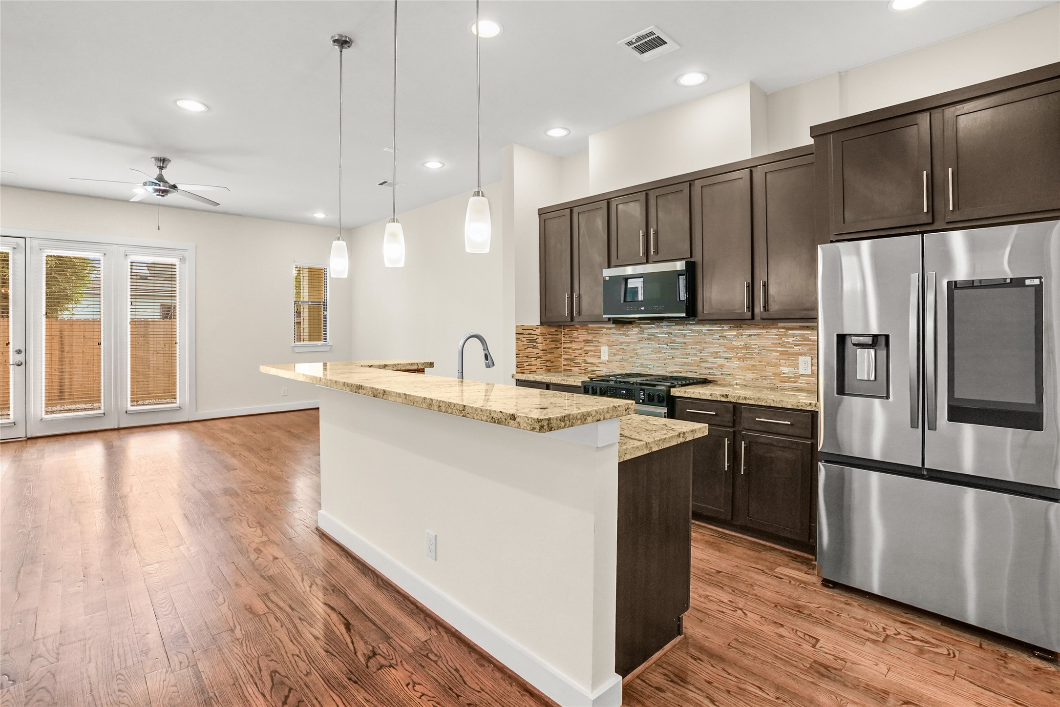 4409 Schuler Street, Unit A Houston, TX 77007 - Photo 8 of 33 The kitchen features a large island with granite countertops and breakfast bar seating, complemented by dark wood cabinetry, stainless steel appliances, and a multi-toned tile backsplash.
