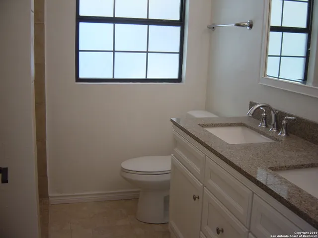 a bathroom with a granite countertop toilet sink and window