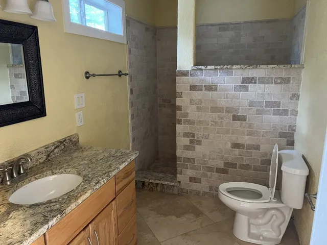 a bathroom with a granite countertop toilet a sink and a mirror