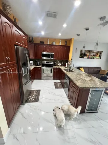 a kitchen with stainless steel appliances kitchen island granite countertop a sink dishwasher stove and refrigerator with wooden cabinets