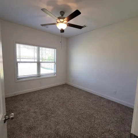 an empty room with a chandelier fan and windows
